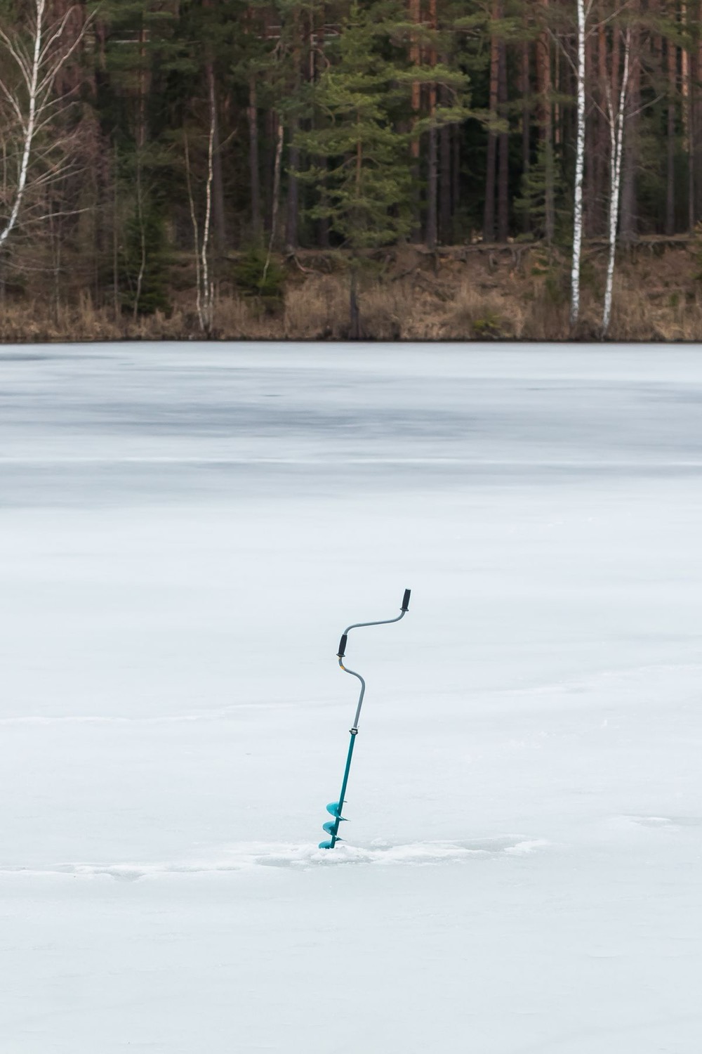 A hand auger standing in the ice on a still frozen lake
