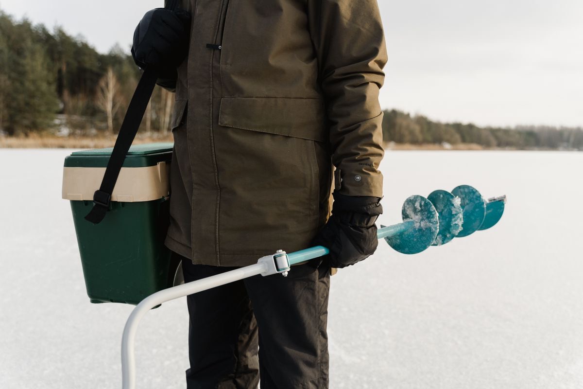 A guide carrying an ice auger and gear box across a frozen lake