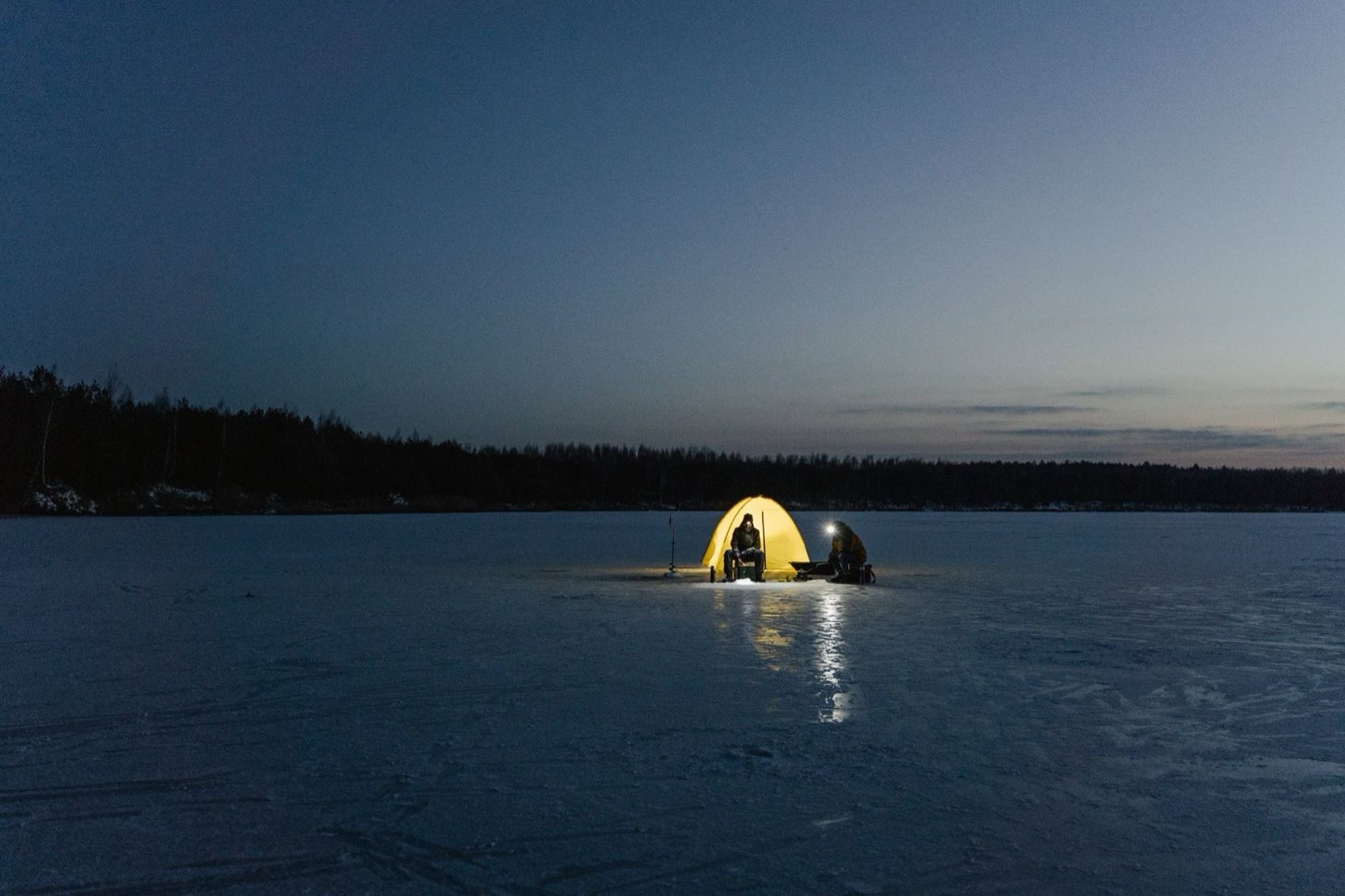 A glowing ice fishing shelter at dusk on a frozen northern lake