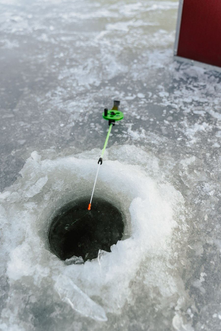 An ice fishing rod set over a freshly drilled hole
