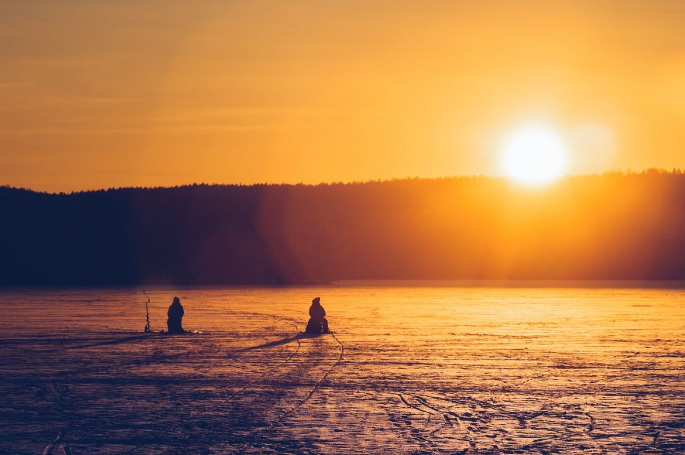 Two anglers silhouetted on a frozen lake at sunset